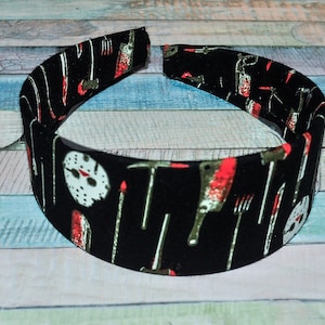 May include: Black headband with a horror movie theme. The headband features a repeating pattern of knives, axes, and a hockey mask.