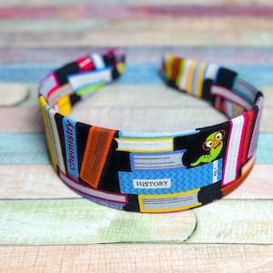 May include: A black headband with a colorful print of stacked books. The print includes the words "chemistry" and "history". A cartoon worm with glasses is on the headband.