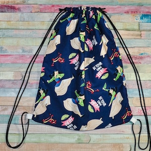 May include: A blue drawstring bag with a repeating pattern of a cartoon woman in a white dress and the text "Be Your Own Hero".