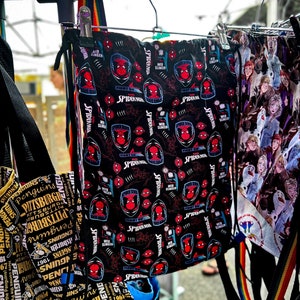 May include: Two drawstring bags hanging on a rack. The bag on the left is yellow and black with the text "Pittsburgh Penguins" repeated. The bag on the right is black with a red Spiderman pattern.