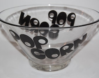 Op de afbeelding: Een glazen kom met zwarte letters die "popcorn" lezen in een retro-lettertype.