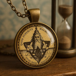 Peut inclure: Pendentif de collier en laiton antique avec une illustration détaillée d'une figure barbue dans un cercle, avec du texte sur les bords. Le pendentif est suspendu à une chaîne assortie. Un sablier est en arrière-plan.
