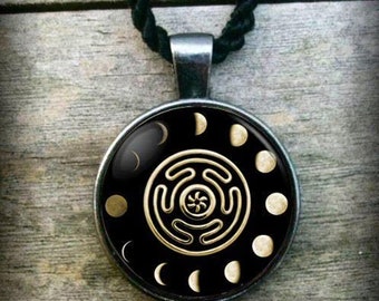 May include: A black pendant necklace with a silver chain and a round glass pendant. The pendant features a gold design of a circle with a spiral in the centre, surrounded by a ring of crescent moons.