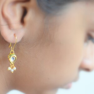 May include: Gold dangle earrings with a teardrop-shaped stone and small pearl accents.