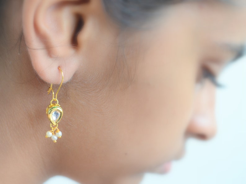 May include: Gold dangle earrings with a teardrop-shaped stone and small pearl accents.