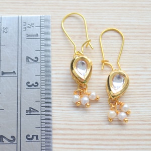 May include: A pair of gold earrings with teardrop-shaped clear stones and small pearl accents. The earrings are approximately 1 1/2 inches long.