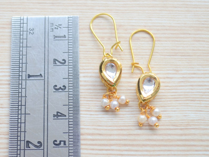 May include: A pair of gold earrings with teardrop-shaped clear stones and small pearl accents. The earrings are approximately 1 1/2 inches long.