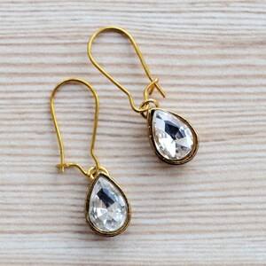 May include: A pair of gold teardrop earrings with clear crystal stones.