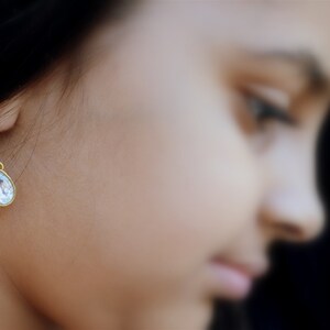 May include: A single teardrop-shaped earring with a clear crystal stone and a gold-toned setting.