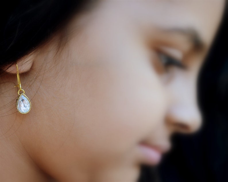 May include: A single teardrop-shaped earring with a clear crystal stone and a gold-toned setting.