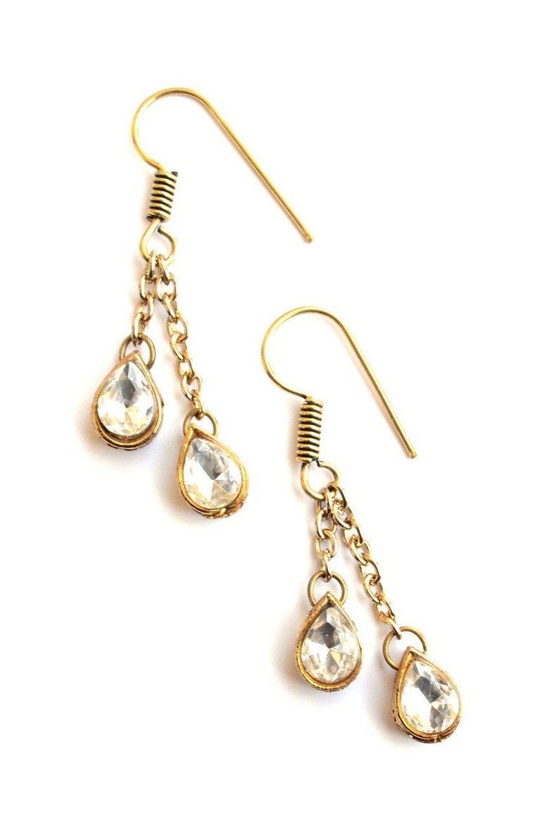 May include: Gold tone dangle earrings with clear teardrop shaped crystals. The earrings have two chains with a crystal at the end of each chain.