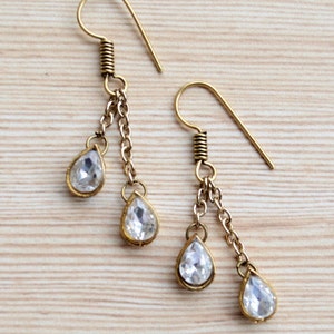 May include: A pair of gold tone dangle earrings with clear teardrop shaped crystals. The earrings have a hook closure.