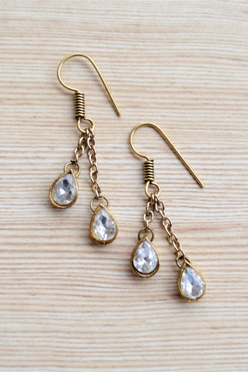 May include: A pair of gold tone dangle earrings with clear teardrop shaped crystals. The earrings have a hook closure.