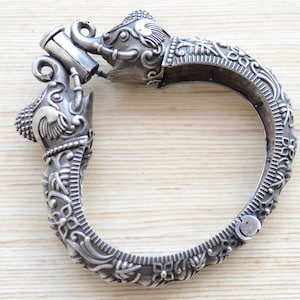Peut inclure: Un bracelet en argent avec deux têtes d'éléphant aux extrémités. Le bracelet est décoré de motifs floraux complexes.
