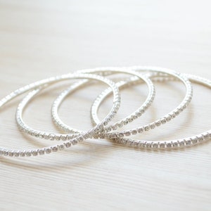 Könnte beinhalten: Set aus vier silberfarbenen Armreifen mit klaren Strasssteinen.