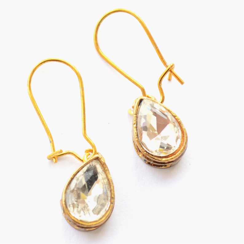 May include: A pair of gold teardrop earrings with clear crystal stones.