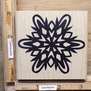 May include: A wooden mounted rubber stamp with a black snowflake design. The stamp measures 2 inches by 2 inches.