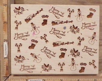 May include: Wooden stamp featuring a repeating pattern of Christmas motifs. The design includes candy canes, snowmen, stockings, bells, bows, and the text "Merry Christmas". The stamp is approximately 13 cm in length.