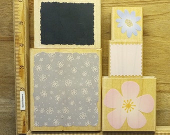 May include: A collection of wooden stamps with floral and rectangular designs. The stamps feature a variety of patterns, including a black rectangle, a floral pattern, and a pink flower. The stamps are arranged on a wooden surface with a ruler.