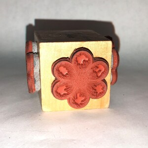 May include: A wooden block with a red flower design on the front and several smaller red stamps on the sides.
