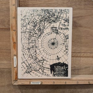 May include: A rectangular wooden stamp featuring a detailed black and white map of the Arctic region. The map includes lines of latitude and longitude, with the words "NORTH" and "EASTERN OCEAN" visible. The stamp is measured with a ruler in inches.