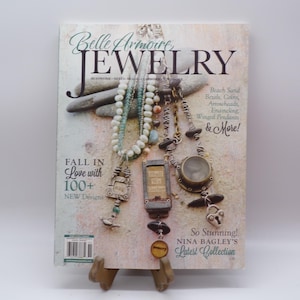 May include: A magazine titled Belle Armoire Jewelry featuring three necklaces with beads, metal charms, and a circular pendant. The cover text includes "Fall in Love with 100+ New Designs" and "Beach Sand, Bezels, Coins, Arrowheads, Enameling, Winged Pendants & More!"