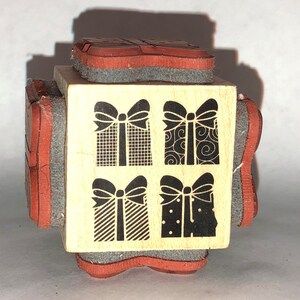 May include: A wooden block with four different designs of gift boxes with bows. Each design features a different pattern: plaid, swirls, stripes, and polka dots.