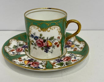 May include: A green and gold teacup and saucer set with floral and fruit designs. The cup and saucer are decorated with a delicate floral pattern and gold accents.