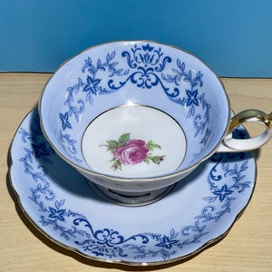 May include: A vintage teacup and saucer set. The cup and saucer are pale blue with detailed dark blue floral patterns and gold edging. A pink rose is in the cup's centre. The handle has a gold accent.