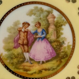 May include: A vintage porcelain plate with a gold rim and a painted scene of a couple in a garden. The scene is signed "Fragonard" in the lower right corner.