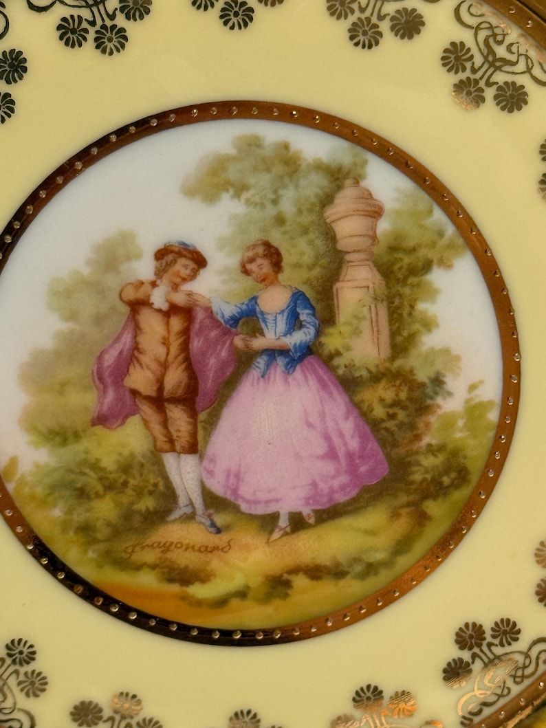 May include: A vintage porcelain plate with a gold rim and a painted scene of a couple in a garden. The scene is signed "Fragonard" in the lower right corner.