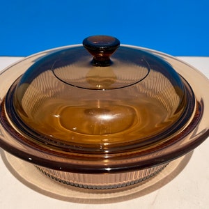 Może przedstawiać: Naczynie do pieczenia ze szkła brązowego z pokrywką. Naczynie ma falisty brzeg, a pokrywka ma gałkę.