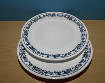 May include: Two white ceramic plates with a blue floral pattern around the rim. The plates are stacked on top of each other.
