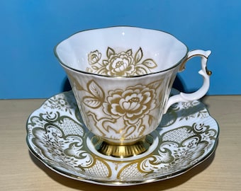 May include: A white teacup and saucer with a gold floral pattern. The cup has a scalloped rim and a delicate handle. The saucer has a matching pattern.