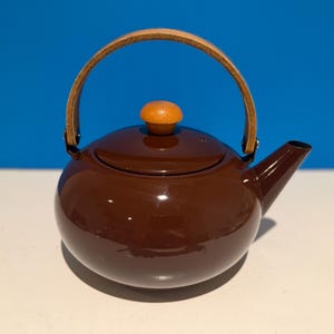 May include: A brown teapot with a wooden handle and a wooden knob on the lid. The teapot has a glossy finish and a spout for pouring. The handle is made of light brown leather.