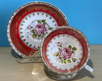 Pode incluir: Um conjunto de chá vintage de xícara e pires com um padrão floral vermelho e dourado. A xícara e o pires apresentam um delicado design floral com rosas cor-de-rosa e folhas verdes. A borda do pires tem uma borda dourada.