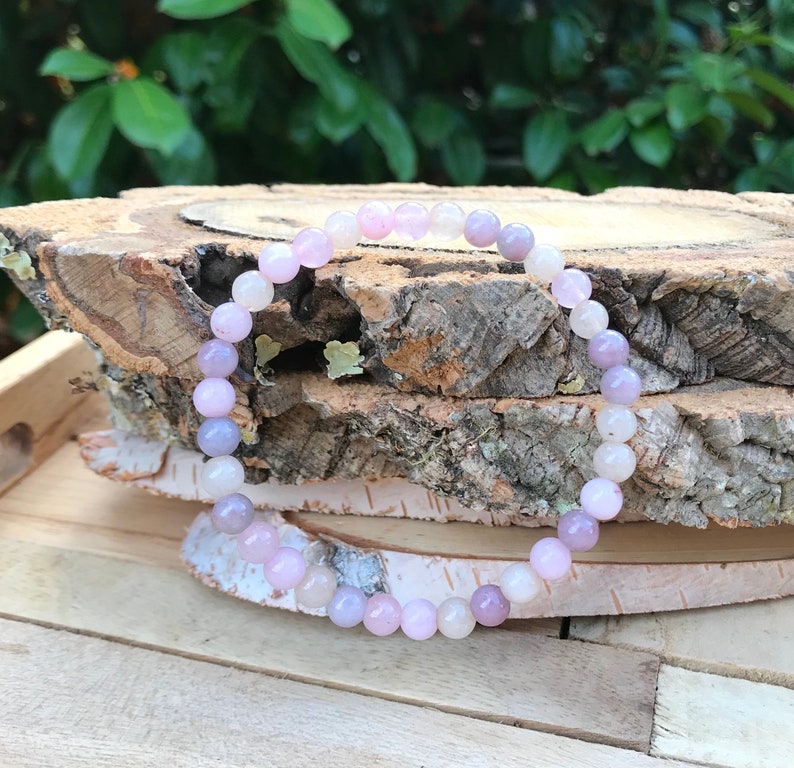 May include: A bracelet made of pink, purple, and white gemstone beads. The bracelet is on a wooden surface.