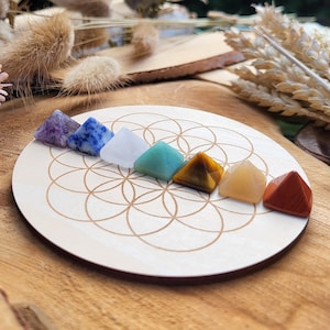 Könnte beinhalten: Sieben Chakra-Pyramidenkristalle in einer Reihe auf einer Holzbasis mit einem Blumenmuster angeordnet. Die Kristalle sind Amethyst, Sodalith, klarer Quarz, Aventurin, Tigerauge, Citrin und roter Jaspis.