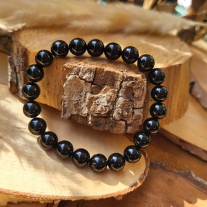 Op de afbeelding: Een zwarte kralen armband gemaakt van ronde, gepolijste stenen. De armband ligt op een houten oppervlak.