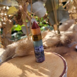 May include: A seven chakra tower made of layered gemstones. The tower is red, orange, yellow, green, blue, indigo, and violet. It is standing on a wooden surface.