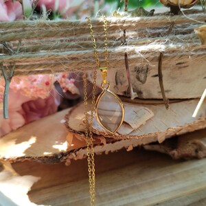 May include: A gold chain necklace with a clear, faceted, teardrop-shaped pendant. The pendant is set in a gold frame and hangs from a delicate gold chain.
