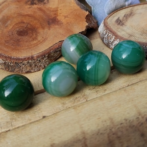 May include: Six green agate spheres with white and green banding. The spheres are arranged on a wooden surface.
