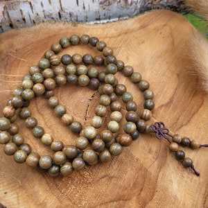 May include: A wooden mala bead necklace with brown and green beads. The necklace is made of natural wood and has a knotted tassel.