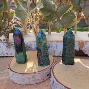 May include: Three green, black and pink gemstone points on wooden bases. The points are polished and have a natural, rough texture.