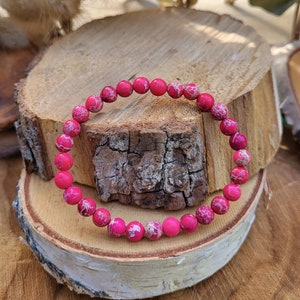 Könnte beinhalten: Ein Armband aus rosa und weißen Edelsteinen auf einem Hintergrund aus Naturholz.