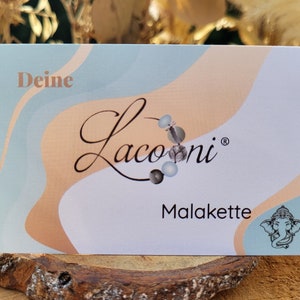 May include: A white card with a blue and peach abstract design. The card has the text "Deine Lacooni&reg; Malakette" and a small image of an elephant.