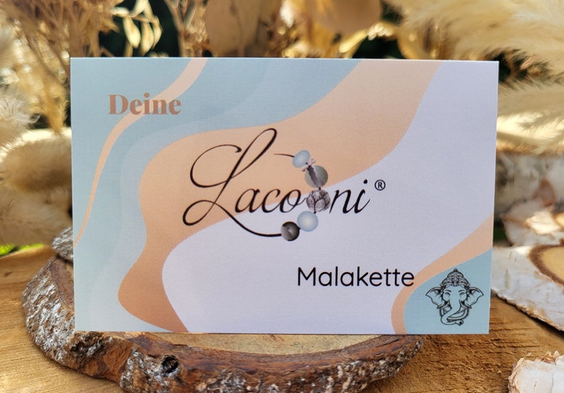 May include: A white card with a blue and peach abstract design. The card has the text "Deine Lacooni&reg; Malakette" and a small image of an elephant.