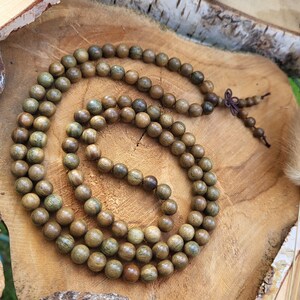 May include: A long strand of brown wooden beads with green accents. The beads are strung together on a thin cord and are arranged in a circular pattern. The beads are lying on a wooden surface.