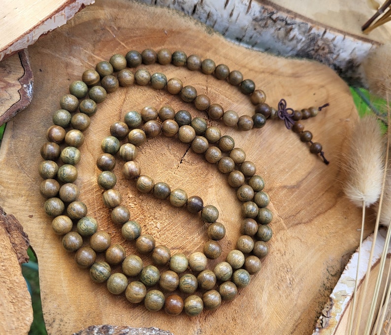 May include: A long strand of brown wooden beads with green accents. The beads are strung together on a thin cord and are arranged in a circular pattern. The beads are lying on a wooden surface.