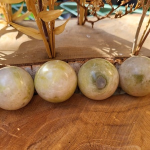 May include: Five smooth, round, green and white gemstone spheres arranged in a row on a wooden surface.